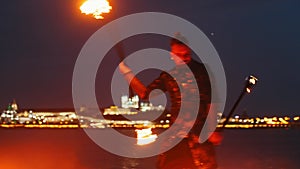 Fire show - a man in shiny costume dancing with two fire torches on the night beach