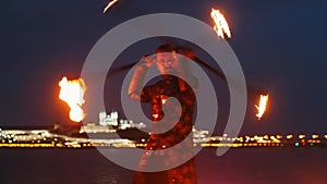 Fire show performance - a man in shiny costume dancing with two fire torches on the night beach