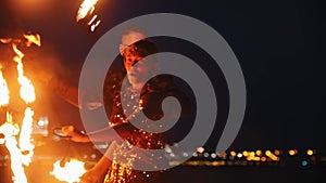 Fire show performance - smiling man and woman in a shiny clothes dancing with fire torches on the night beach