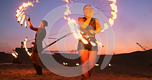 Fire show three women in their hands twist burning spears and fans in the sand with a man with two flamethrowers in slow