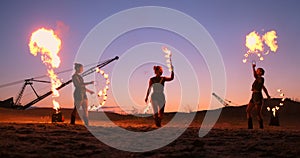 Fire show three women in their hands twist burning spears and fans in the sand with a man with two flamethrowers in slow