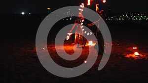 Fire show - two women in shiny dresses synchronously dancing with lit torches on the beach at night