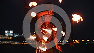 Fire show - woman in a shiny dress and man behind her performing with fire torches on the night beach