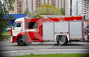 A fire truck is driving an emergency call on a road in the city. side view