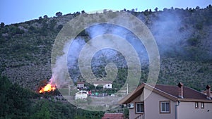 Fire truck with flashing lights stands near a burning house in the mountains