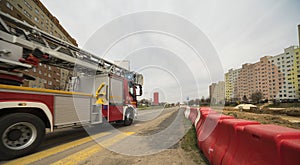 A fire truck with a ladder speeding on its siren through a renovated street.