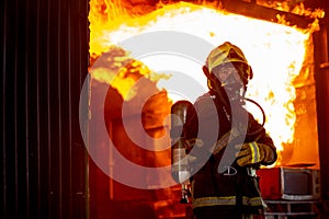 Fire on wall and ceiling in the kitchen behind firefighter man with protective and safety clothes stand with arm-crossed