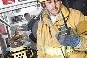 Fire Worker Holding Walkie Talkie With Patient And EMT Doctor In Ambulance