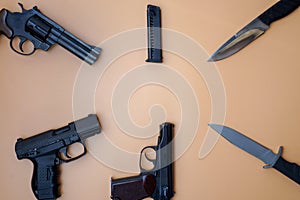 Firearms laid out along a circle. Three guns pistols, cartridges, army knives close-up on a neutral beige background. copy space