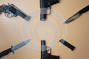 Firearms laid out along a circle. Three guns pistols, cartridges, army knives close-up on a neutral beige background. copy space