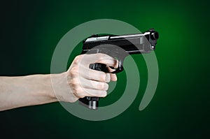 Firearms and murderer topic: human hand holding a gun on a dark green background isolated in studio