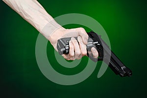 Firearms and murderer topic: human hand holding a gun on a dark green background isolated in studio