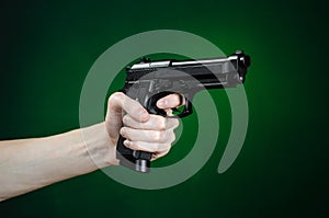 Firearms and murderer topic: human hand holding a gun on a dark green background in studio