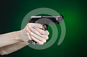 Firearms and murderer topic: human hand holding a gun on a dark green background in studio