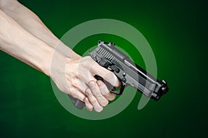 Firearms and murderer topic: human hand holding a gun on a dark green background in studio