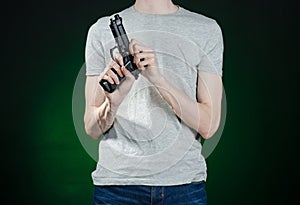 Firearms and murderer topic: man in a gray t-shirt holding a gun on a dark green background isolated in studio