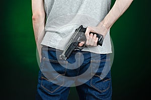 Firearms and murderer topic: man in a gray t-shirt holding a gun on a dark green background in studio