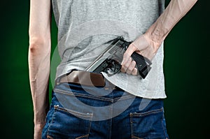 Firearms and murderer topic: man in a gray t-shirt holding a gun on a dark green background in studio