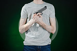 Firearms and murderer topic: man in a gray t-shirt holding a gun on a dark green background in studio