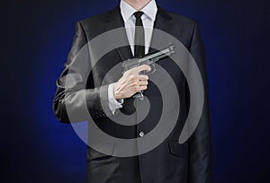 Firearms and security topic: a man in a black suit holding a gun on a dark blue background in studio