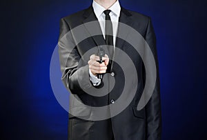 Firearms and security topic: a man in a black suit holding a gun on a dark blue background in studio