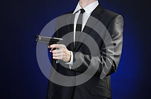 Firearms and security topic: a man in a black suit holding a gun on a dark blue background in studio