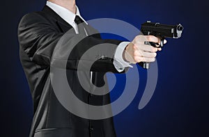 Firearms and security topic: a man in a black suit holding a gun on a dark blue background in studio