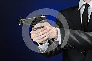 Firearms and security topic: a man in a black suit holding a gun on a dark blue background in studio