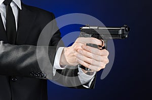 Firearms and security topic: a man in a black suit holding a gun on a dark blue background in studio