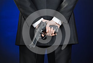 Firearms and security topic: a man in a black suit holding a gun on a dark blue background in studio