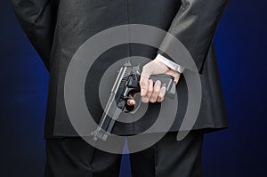 Firearms and security topic: a man in a black suit holding a gun on a dark blue background in studio