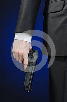 Firearms and security topic: a man in a black suit holding a gun on a dark blue background in studio