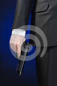 Firearms and security topic: a man in a black suit holding a gun on a dark blue background in studio