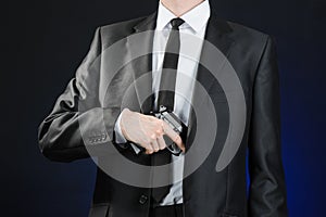 Firearms and security topic: a man in a black suit holding a gun on a dark blue background in studio