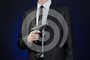 Firearms and security topic: a man in a black suit holding a gun on a dark blue background in studio