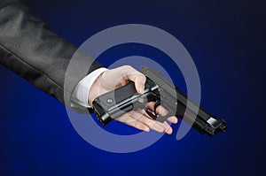 Firearms and security topic: a man in a black suit holding a gun on a dark blue background in studio