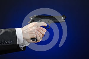 Firearms and security topic: a man in a black suit holding a gun on a dark blue background in studio