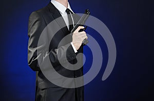 Firearms and security topic: a man in a black suit holding a gun on a dark blue background in studio isolated