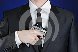 Firearms and security topic: a man in a black suit holding a gun on a dark blue background in studio isolated