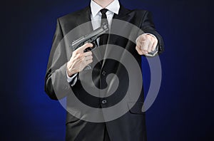 Firearms and security topic: a man in a black suit holding a gun on a dark blue background in studio isolated