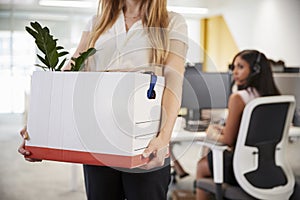 Fired female employee holding box of belongings in an office