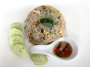 Fired rice with mackerel fish and vegetable serve with fish sauce and cucumber decoration on white dish.