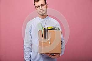 Fired sad guy in blue shirt and glasses holds cardboard box with different things