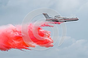 Firefighter airplane drops red water on a fire in the forest.