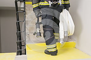 A firefighter climbs the stairs and carries a hose line and equipment for extinguishing fires indoors, rear view