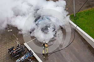 A firefighter creates a lot of smoke and steam when putting out a car in the driveway of a parking garage