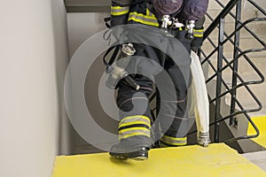 A firefighter descends the stairs and carries a hose line and equipment for extinguishing fires indoors, front view