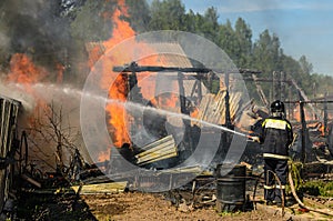 Firefighter extinguishes burning house engulfed in flames using fire hose with water