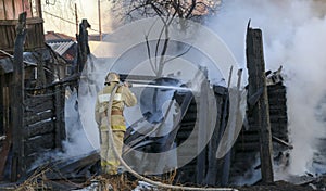 Firefighter extinguishes the fire. Fireman holding hose with water, watering strong stream of burning wooden structure in smoke. photo