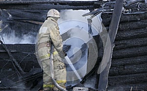 Firefighter extinguishes the fire. Fireman holding hose with water, watering strong stream of burning wooden structure in smoke. photo